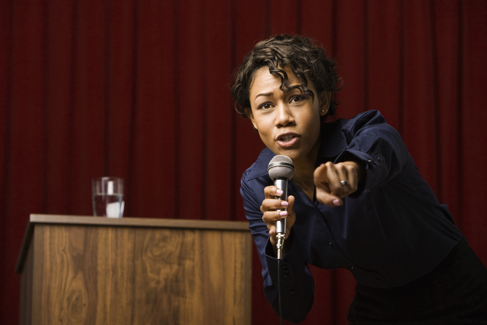Mixed race businesswoman speaking on stage and pointing